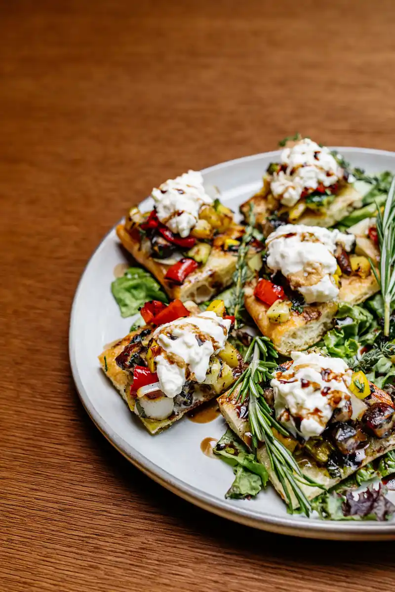 Topped flatbread slices on a plate of greens at Jasper’s